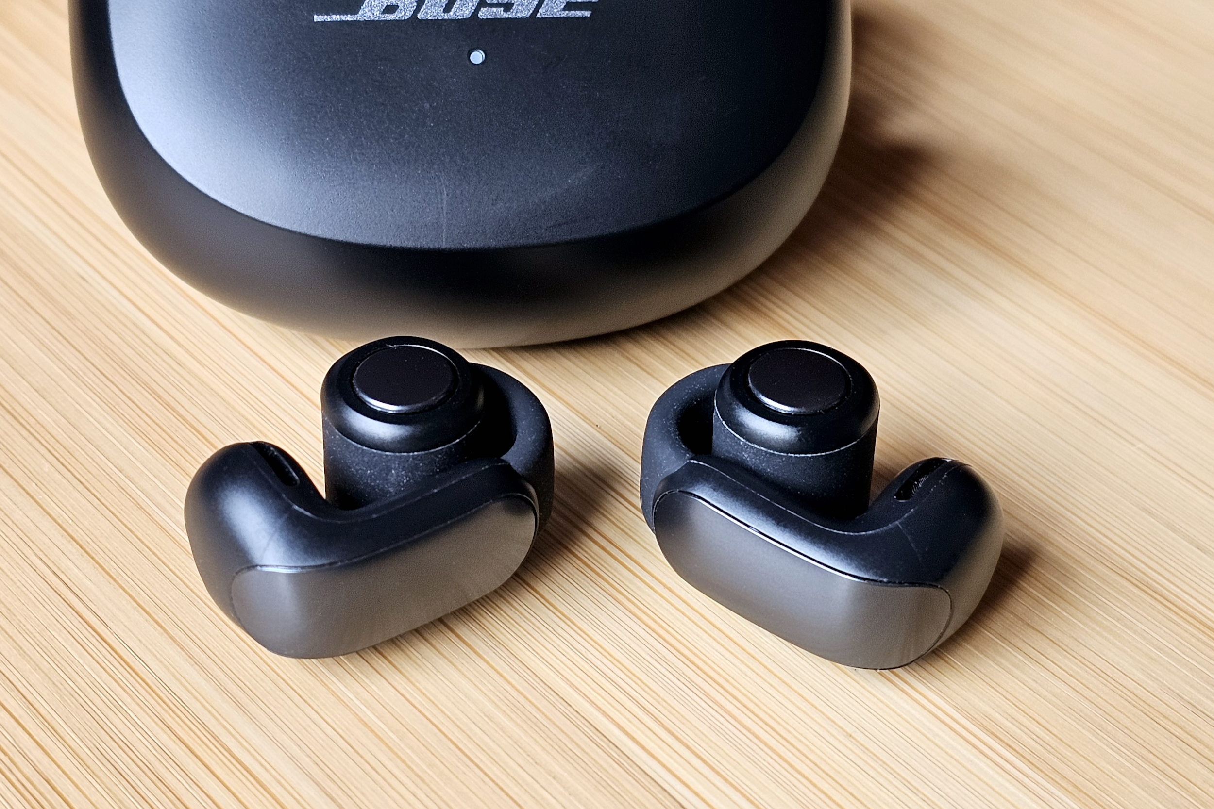 Bose Ultra Open Earbuds in front of their charging case.