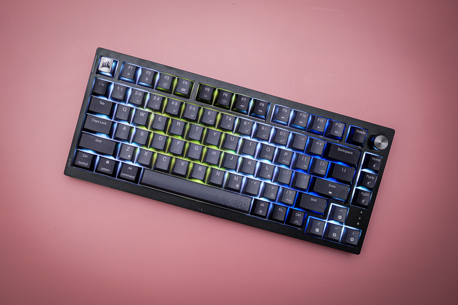 The Corsair K65 Plus Wireless keyboard on a pink background.