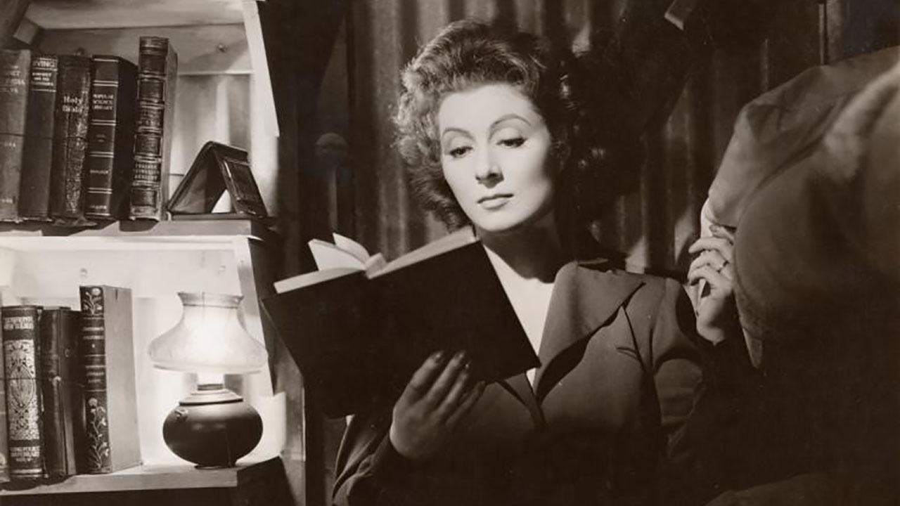 Greet Garson reading a book in a black and white scene from the movie Mrs. Miniver