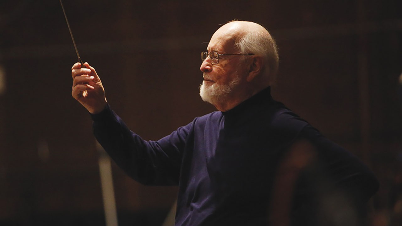 John Williams composing in a side profile on a dark background.
