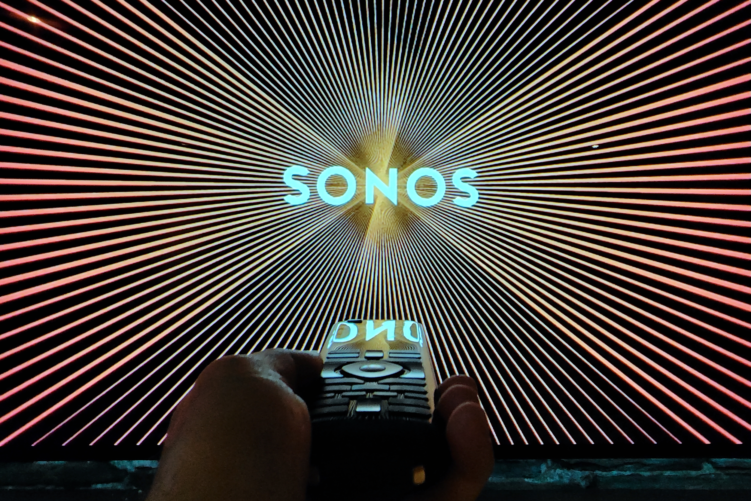 A remote contol pointed at a TV displaying the Sonos logo.