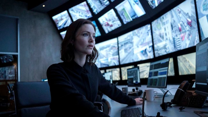 A woman looks at a wall of TV screens in The Capture.
