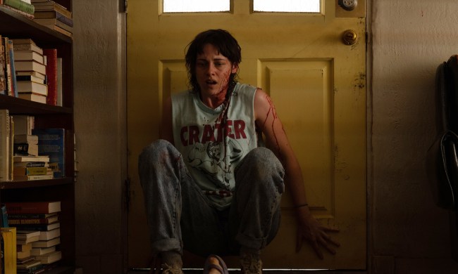 A blood-splattered Kristen Stewart sits against a door in Love Lies Bleeding.