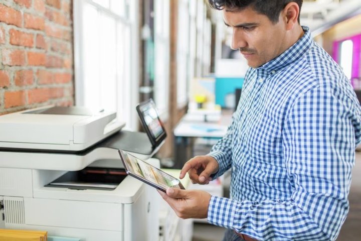 A person uses a tablet with an HP laser printer in an office.