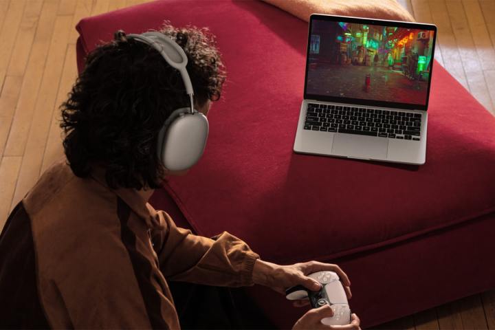 A person plays Stray using a PlayStation controller on a silver 13-inch MacBook Air.
