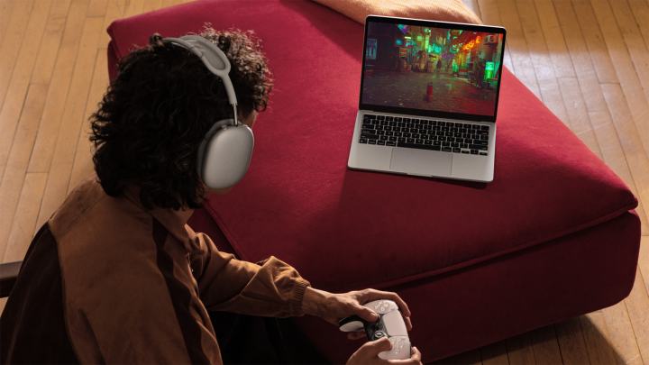 An Apple press photo of someone playing a game on a MacBook Air with a controller.