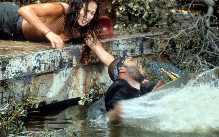 Una serpiente muerde a un hombre en el agua mientras una mujer intenta agarrarlo.