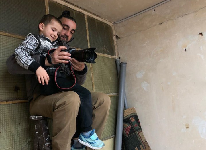 एक फोटोग्राफर अपनी गोद में बैठे एक बच्चे को कैमरा दिखाता है।