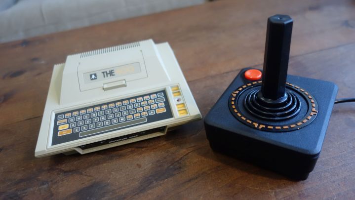 একটি Atari 400 Mini একটি জয়স্টিকের পাশে একটি টেবিলে বসে আছে।
