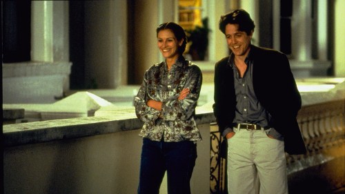 Julia Roberts and Hugh Grant walking down a street together smiling in a scene from Notting Hill.