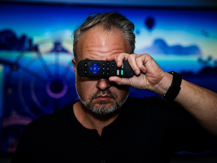 Phil Nickinson holding a Roku remote control over his eyes as the Roku screensaver plays behind him.