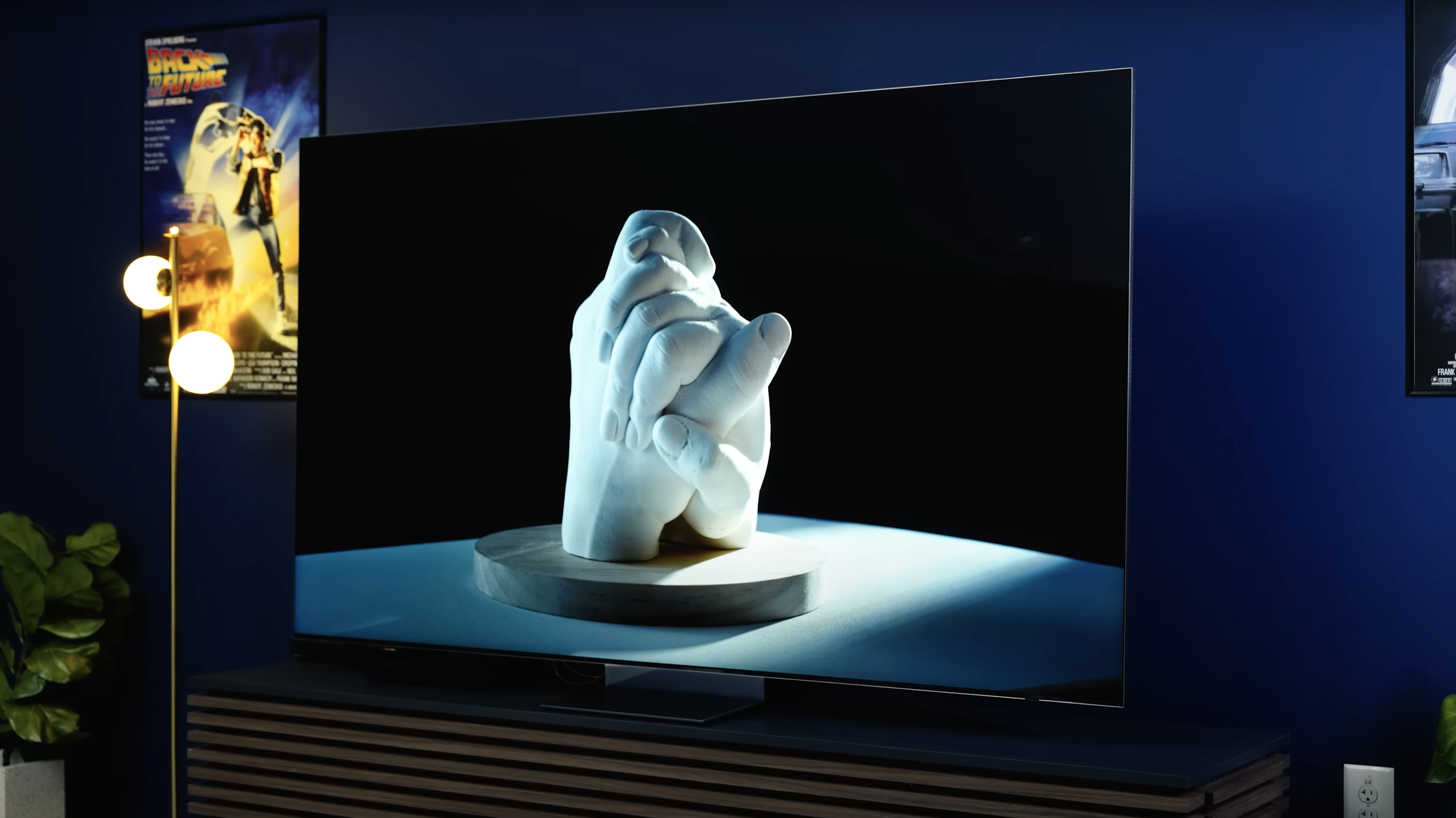 A sculpture of two clasped hands is shown on a Samsung QN900D.