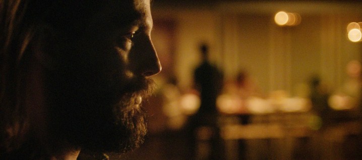 A man looks on as a party happens behind him in The Invitation.