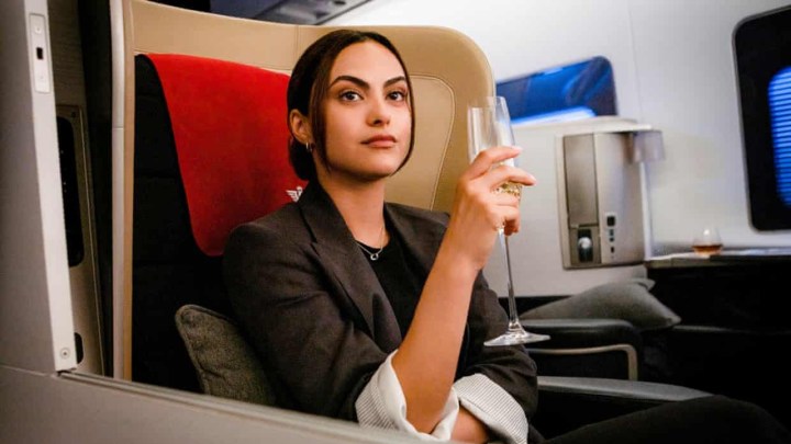 Camilla Mendes as Ana in Upgraded, sitting in first class with a glass of champagne.