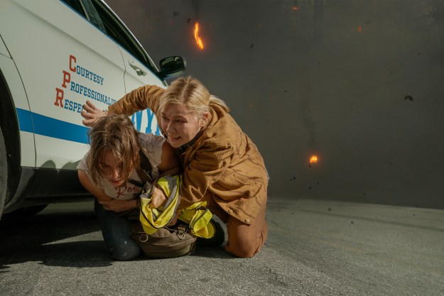 Cailee Spaeny and Kirsten Dunst crouch next to a car in Civil War.