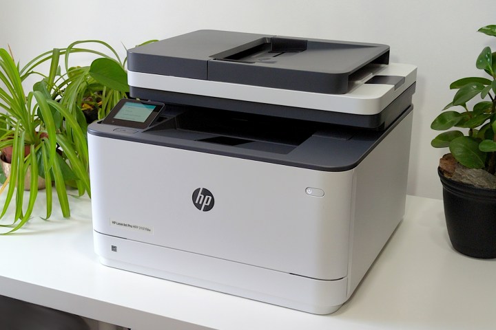 چاپگر HP LaserJet Pro MFP 3101fdw روی پایه سفید در کنار گیاهان خوب به نظر می رسد.