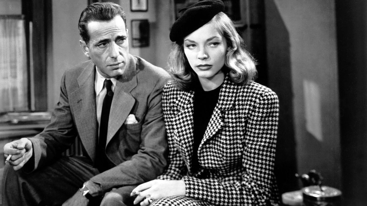 Humphrey Bogart y Lauren Bacall como Philip Marlowe y Vivien Sternwood Rutledge sentados uno al lado del otro en The Big Sleep.