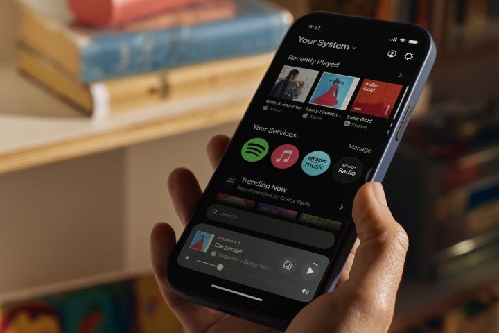 A hand-held iPhone showing the new Sonos app's home screen.