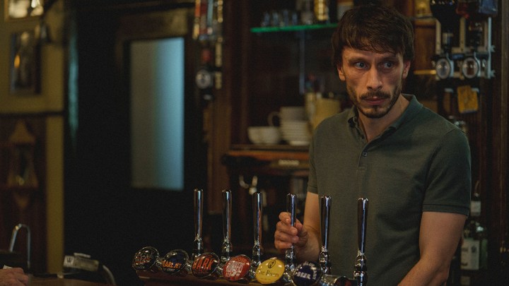 A man standing behind a bar, glancing to his side in a scene from Baby Reindeer on Netflix.