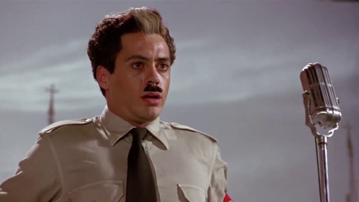 Robert Downey Jr. como Charlie Chaplin en Chaplin vistiendo un uniforme con un pequeño bigote y una mirada aturdida.