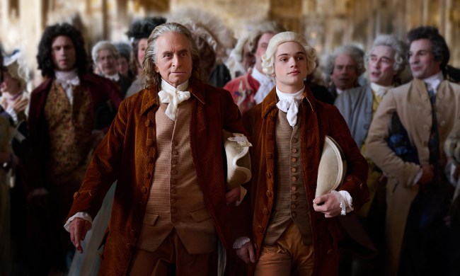 Michael Douglas as Benjamin Franklin and Noah June as his grandson walking in full historical garb, people behind them in a scene from the Apple TV+ series Franklin.