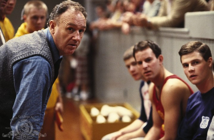 A man leans over to talk to three guys in Hoosiers.
