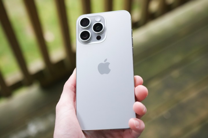 Кто-то держит iPhone 15 Pro Max снаружи, во внутреннем дворике, с обратной стороной цвета Natural Titanium.