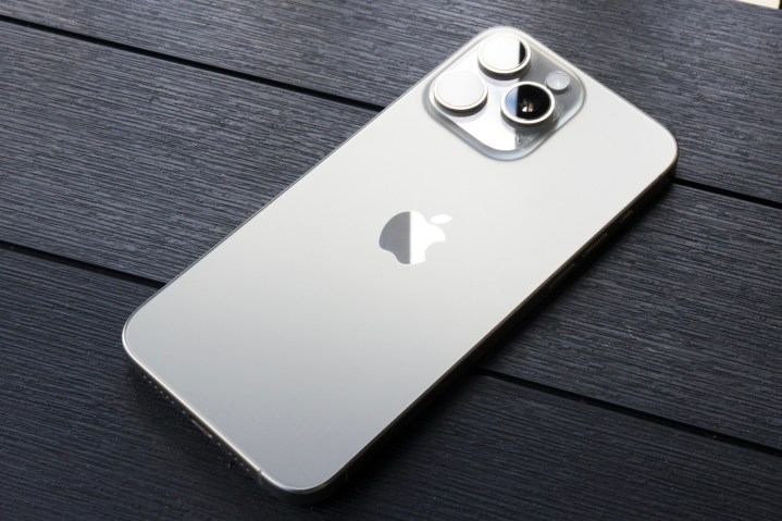 Ан iPhone 15 Pro Max лежит лицом вниз снаружи, показывая цвет натурального титана.