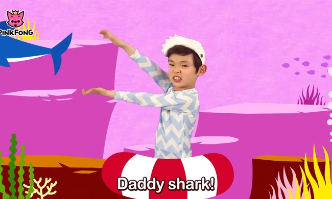 A child stretching and moving his arms like a shark's mouth with animation behind him in the Pinking Baby Shark video on YouTube.