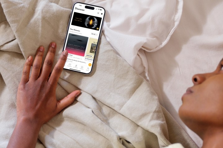 一个人躺在床上，旁边的手机打开了 Qobuz 应用程序。