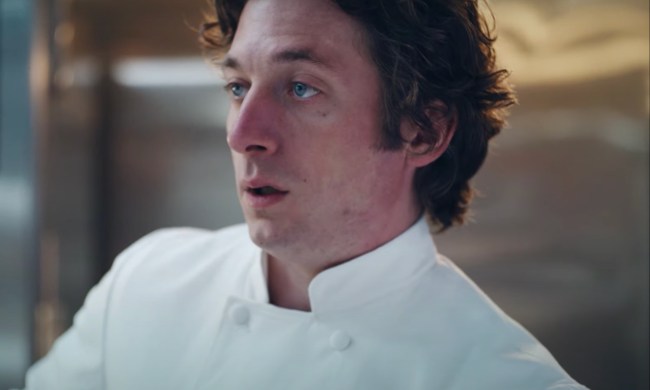 A man in a chef's coat looks to someone off-screen.