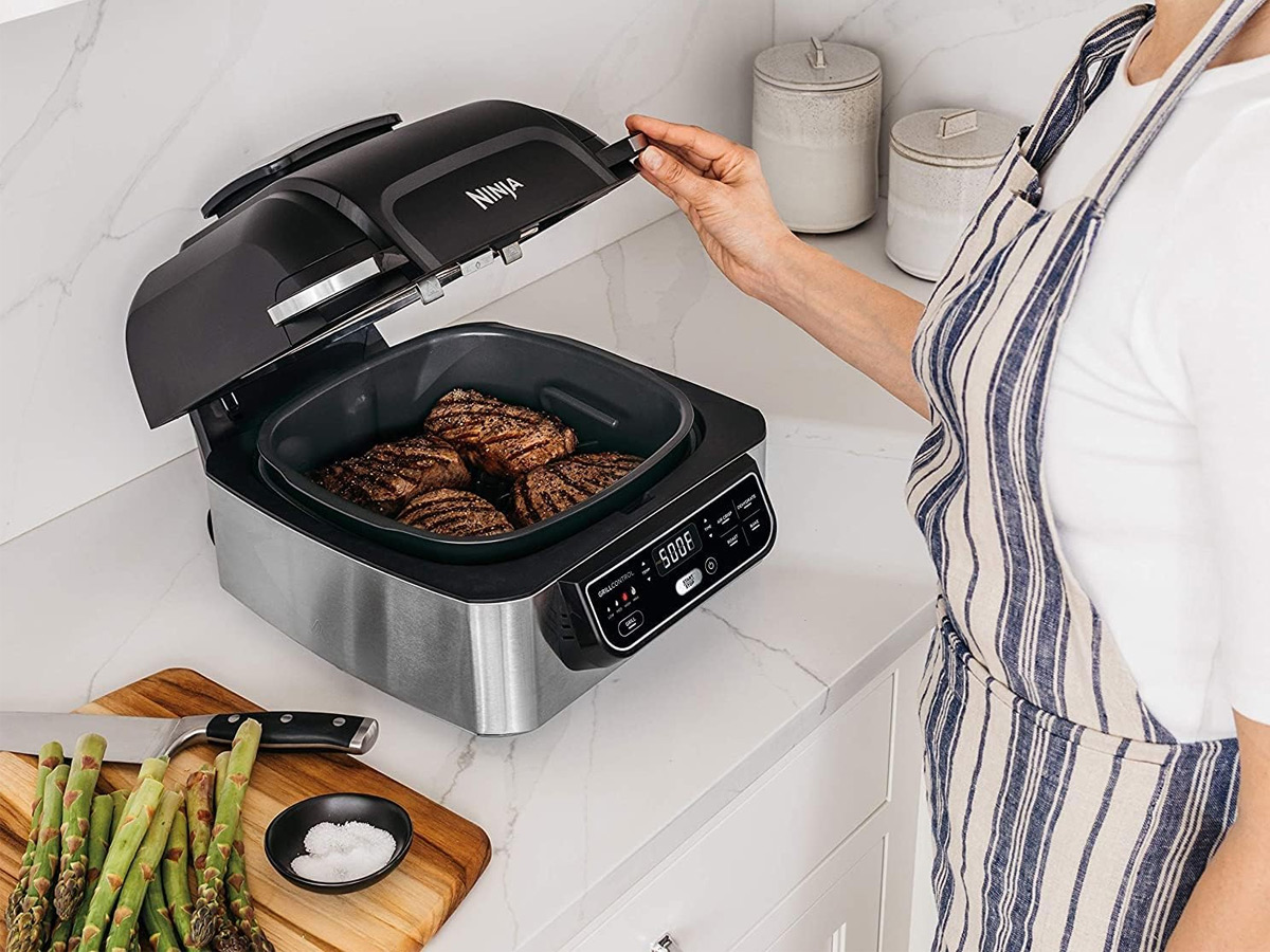 A woman looks at the food cooking in the Ninja Foodi 5-in-1 indoor electric grill.