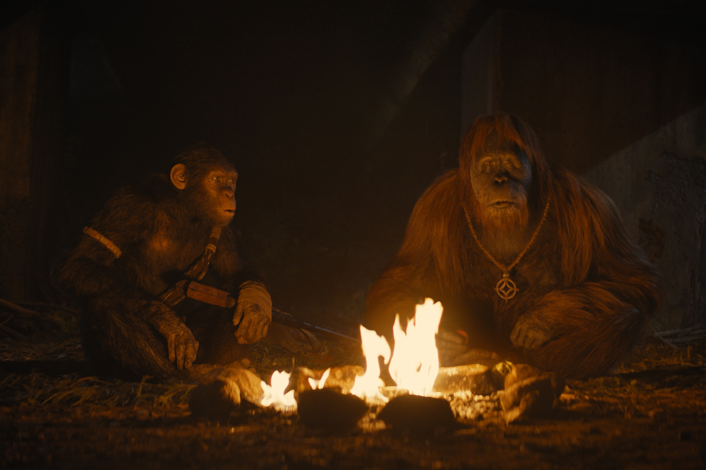 Noa and Raka sit near a campfire together in Kingdom of the Planet of the Apes.