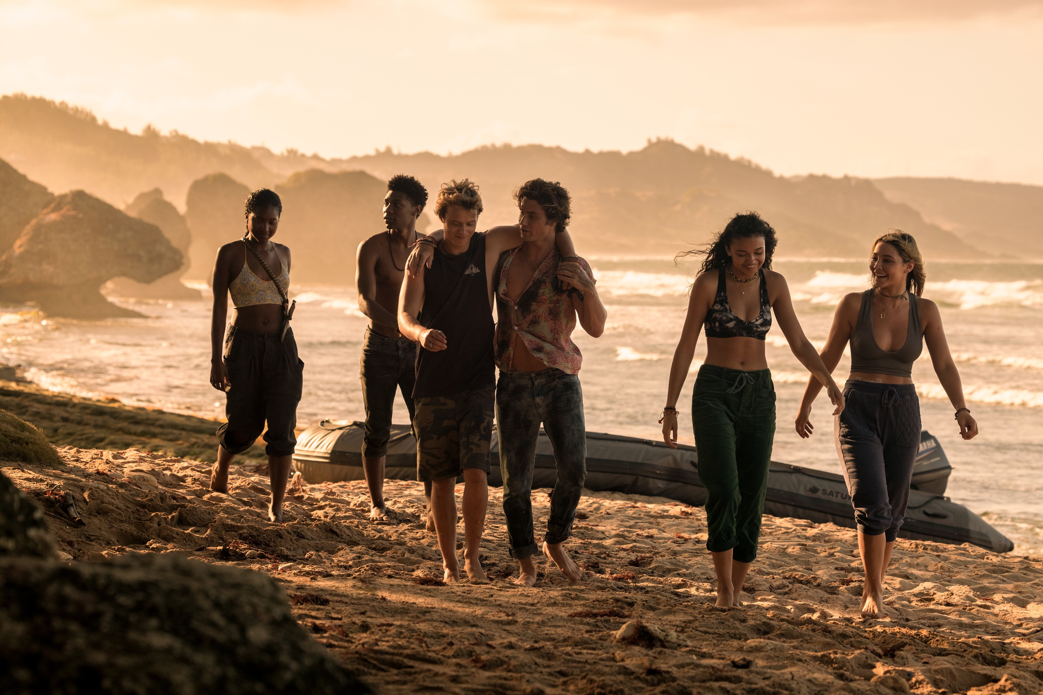 A group of teenagers walk alongside a beach.