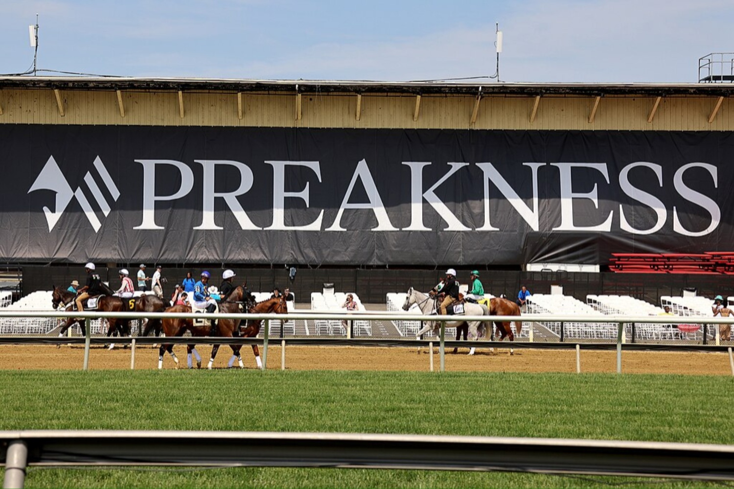 Horse on the track trot in front of the Preakness Stakes sign.