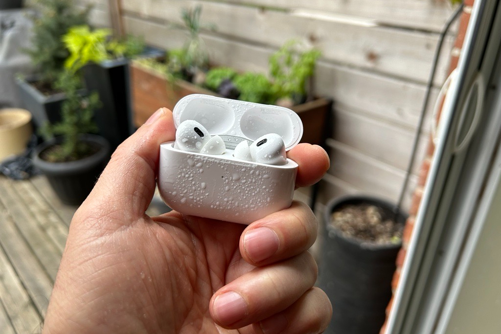 A pair of Apple AirPods Pro in an open case with water splashed on them.