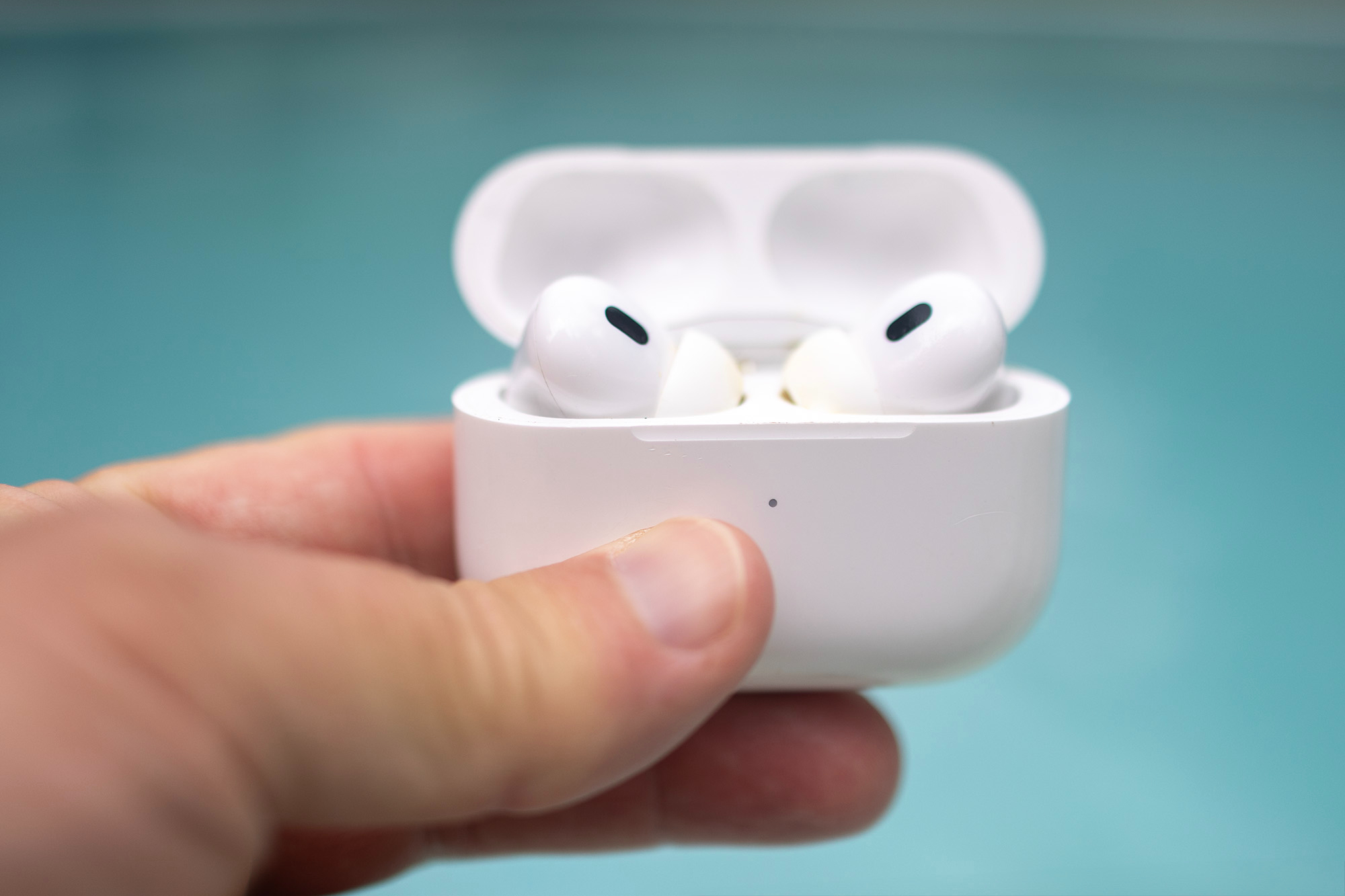 A pair of Apple AirPods Pro in an open case with a swimming pool in the background.