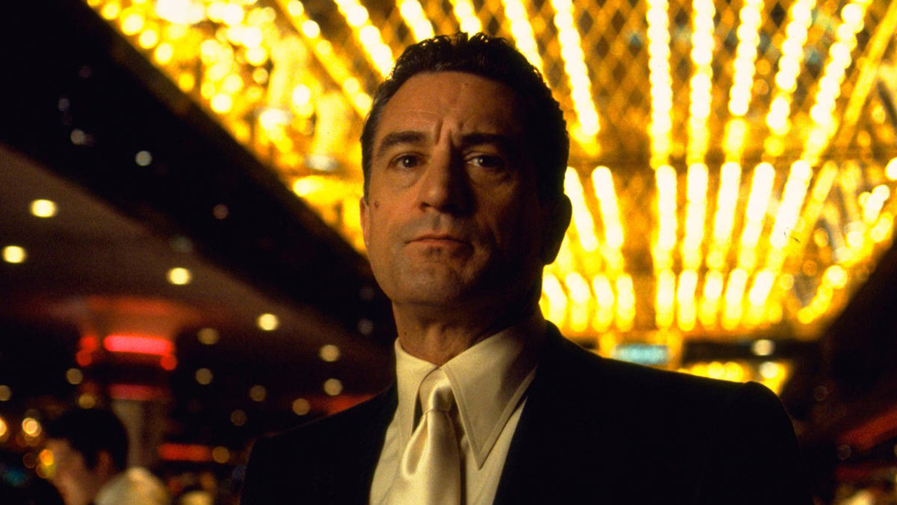 An underhand shot of Robert DeNiro in the movie Casino standing in a suit in the casino looking serious.