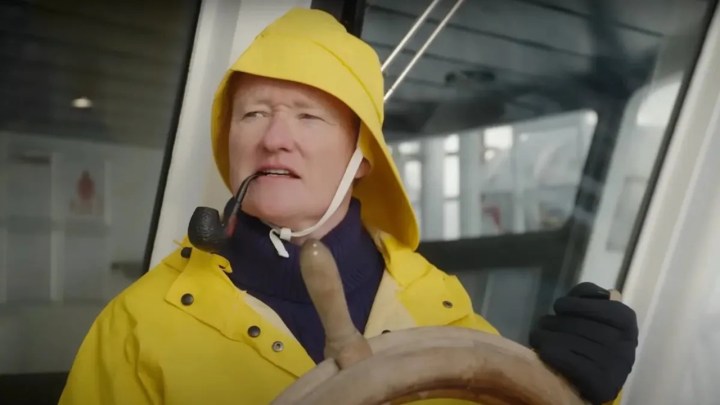 Conan O'Brien behind the wheel of a boat wearing a yellow rain jacket with a pipe in his mouth in a scene from Conan O'Brien Must Go.